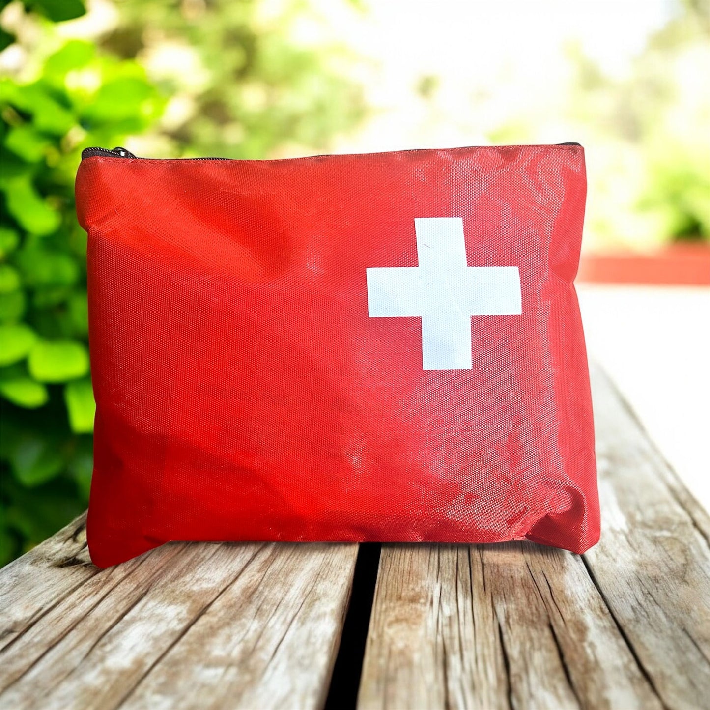 Red first aid kit with a white cross on a wooden surface outdoors