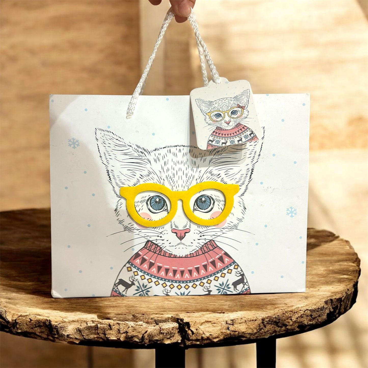 Greeting card with a cat illustration wearing yellow glasses and a pink sweater on a wooden surface.