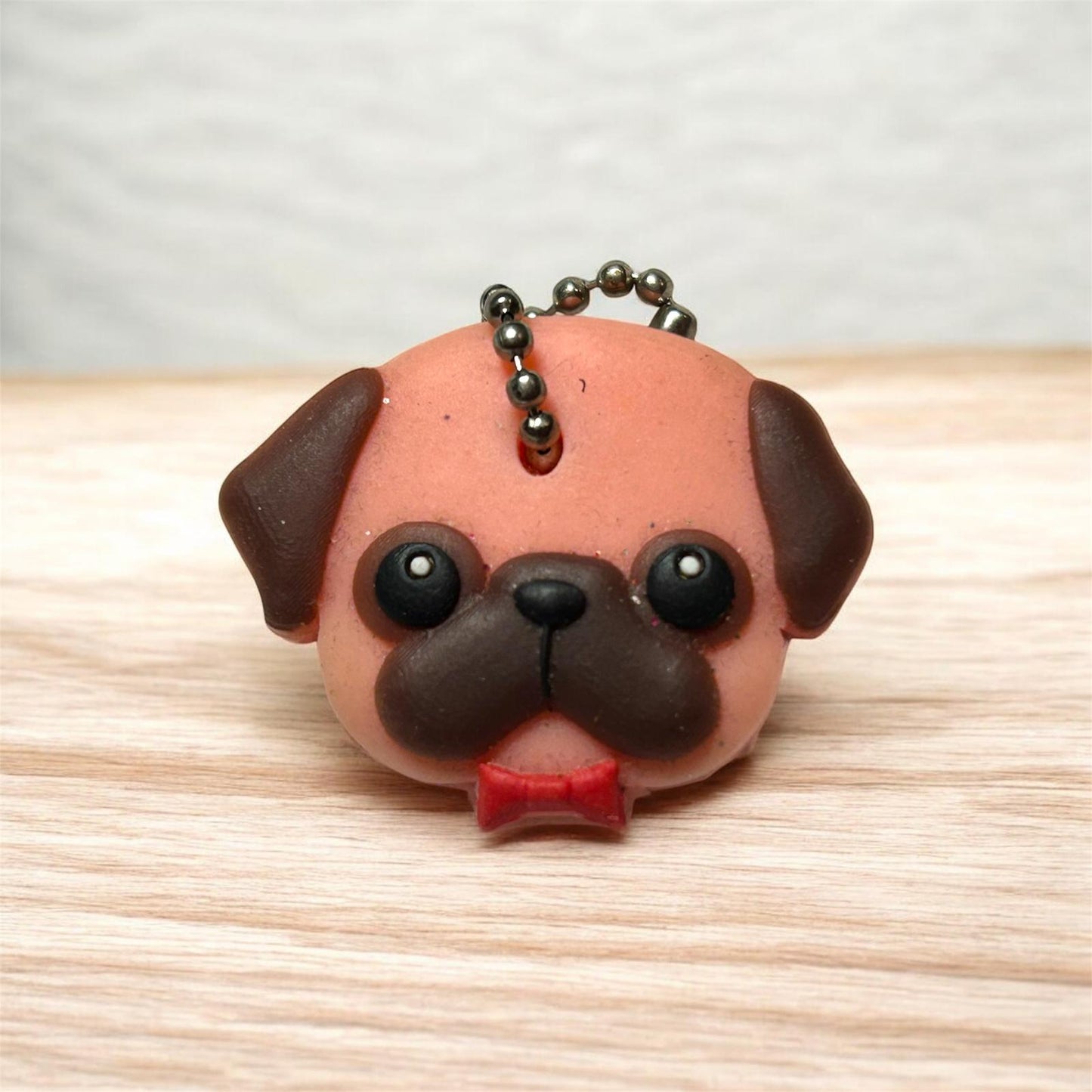 Dog-shaped keychain with a red bow tie on a wooden surface
