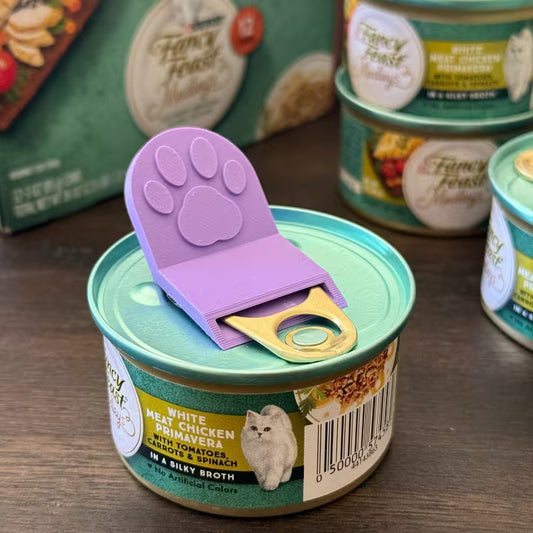 Pet food can opener with paw design on a cat food can, surrounded by more cans in the background.