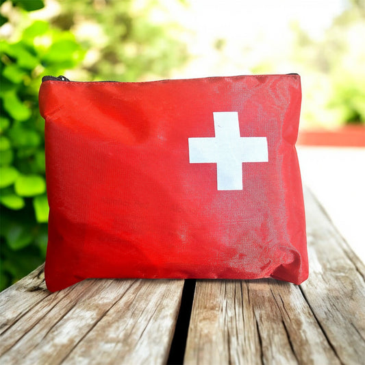 Red first aid kit with a white cross on a wooden surface outdoors