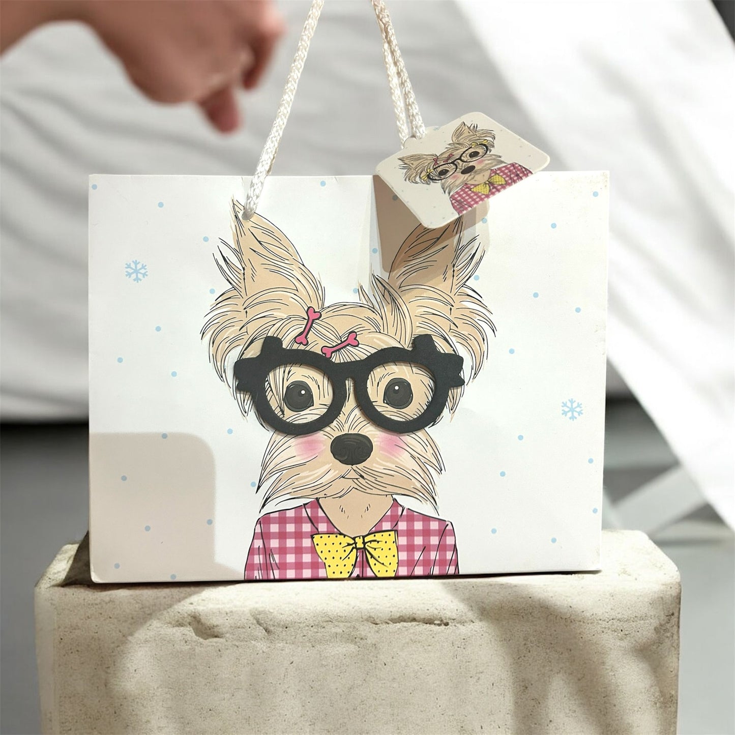 Card with a dog illustration wearing glasses and a bow tie, held by a hand.