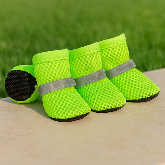 Four bright green dog boots with reflective straps on a wooden surface with grass in the background.